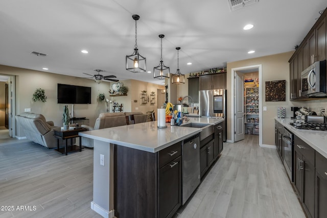 kitchen with hanging light fixtures, appliances with stainless steel finishes, a kitchen island with sink, and dark brown cabinetry