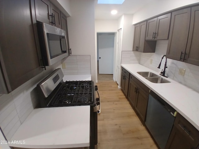 kitchen with decorative backsplash, appliances with stainless steel finishes, a skylight, sink, and light hardwood / wood-style floors