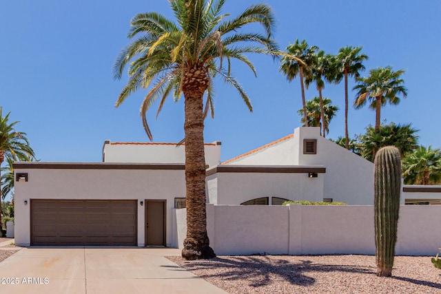 mid-century home featuring an attached garage, stucco siding, fence, and driveway