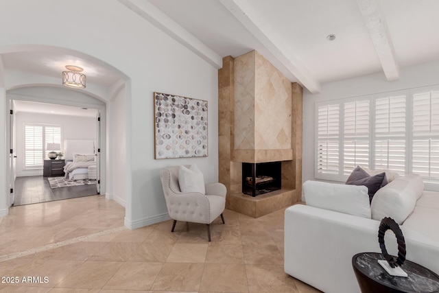 living room featuring baseboards, vaulted ceiling with beams, a tile fireplace, arched walkways, and light tile patterned floors