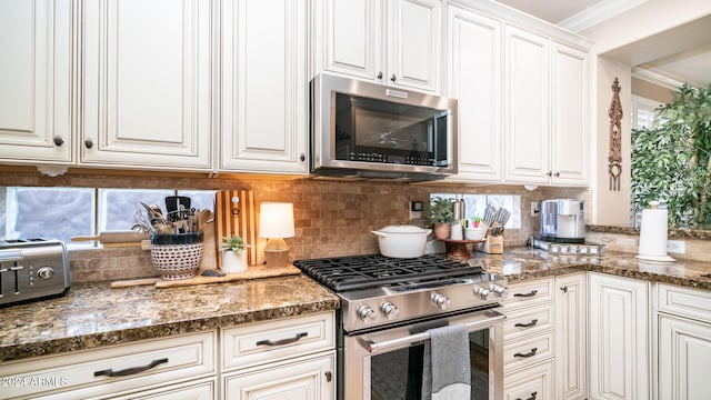 kitchen featuring decorative backsplash, appliances with stainless steel finishes, white cabinetry, dark stone countertops, and crown molding