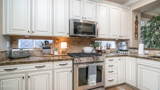 kitchen featuring appliances with stainless steel finishes, white cabinetry, dark stone counters, crown molding, and decorative backsplash