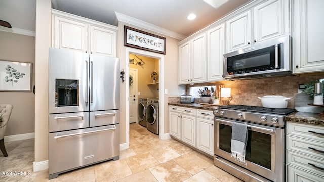 kitchen with appliances with stainless steel finishes, white cabinets, dark stone countertops, and washer and clothes dryer