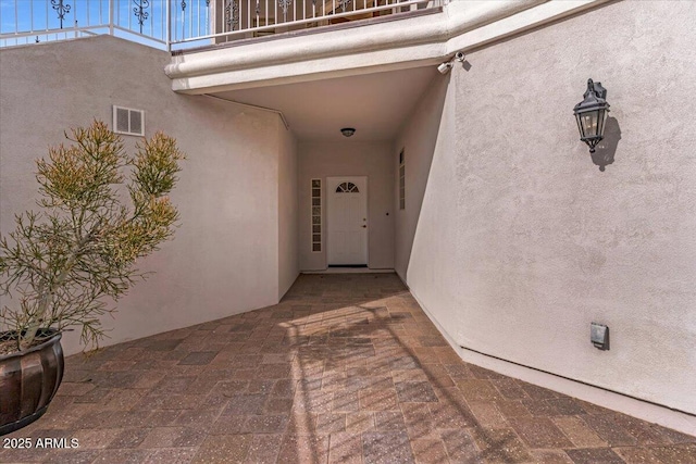 property entrance featuring a balcony, visible vents, and stucco siding