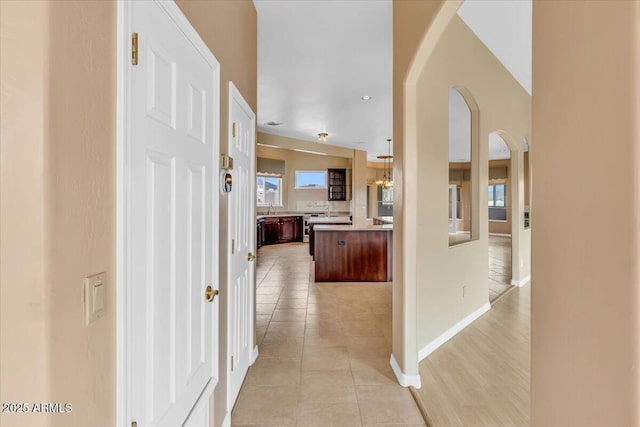 hallway with arched walkways, a sink, baseboards, and light tile patterned floors