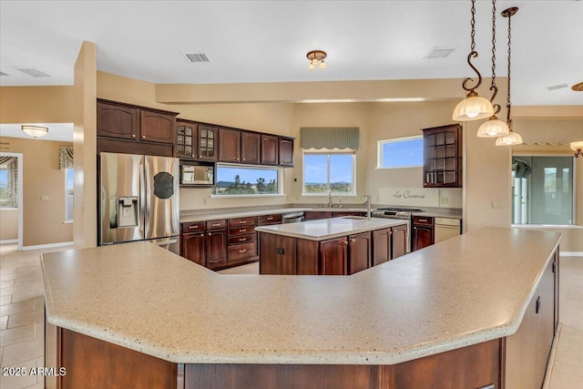 kitchen featuring stainless steel appliances, a spacious island, light countertops, visible vents, and glass insert cabinets