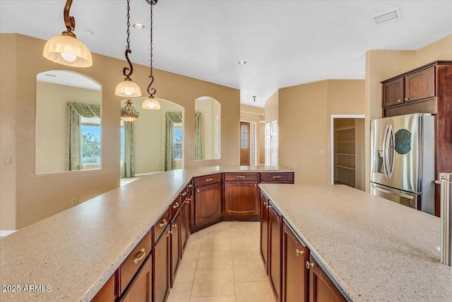 kitchen featuring light tile patterned floors, visible vents, light stone counters, decorative light fixtures, and stainless steel refrigerator with ice dispenser