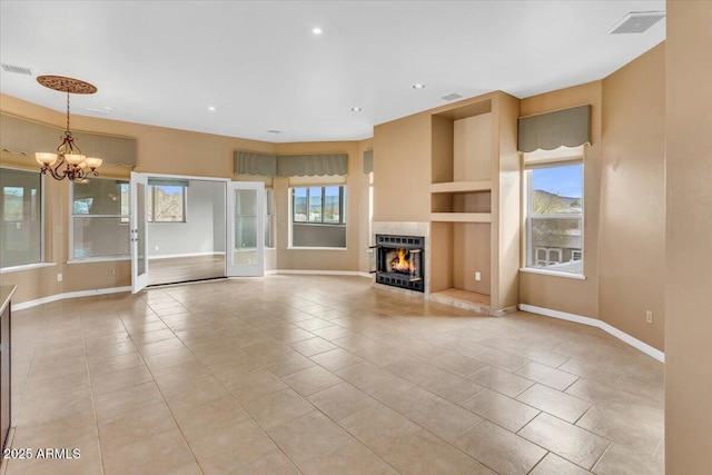 unfurnished living room with light tile patterned floors, visible vents, baseboards, a lit fireplace, and a notable chandelier