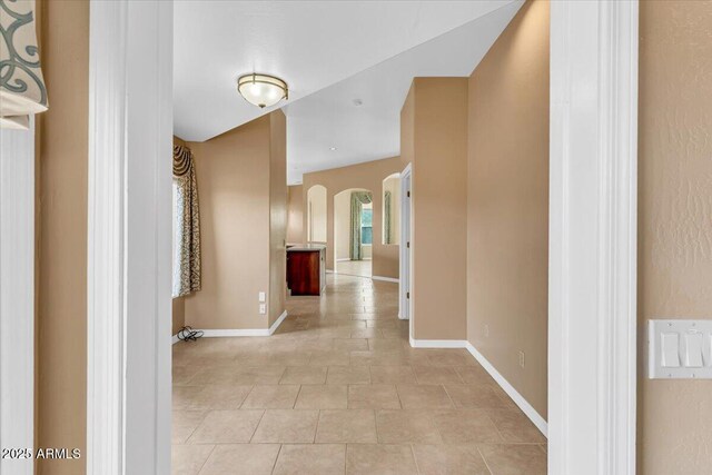 corridor featuring arched walkways and baseboards