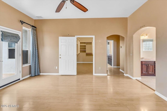 empty room with arched walkways, ceiling fan, light wood-style flooring, visible vents, and baseboards