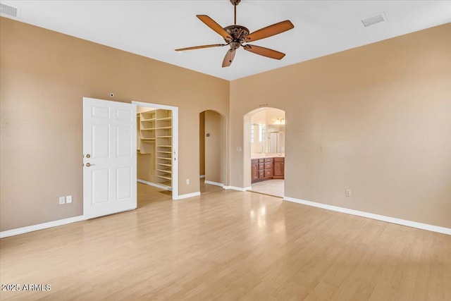 unfurnished room with light wood-type flooring, arched walkways, visible vents, and baseboards