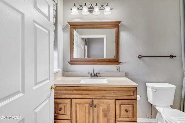 bathroom with toilet, a textured wall, and vanity