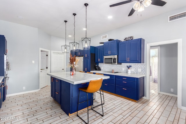 kitchen featuring a kitchen bar, appliances with stainless steel finishes, blue cabinets, decorative light fixtures, and a center island