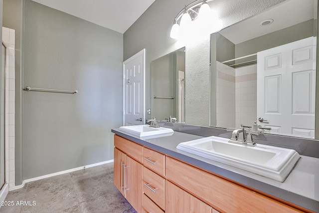 bathroom featuring double vanity, tiled shower, baseboards, and a sink
