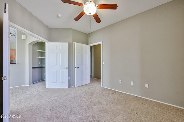 unfurnished bedroom with baseboards, arched walkways, carpet floors, and ceiling fan