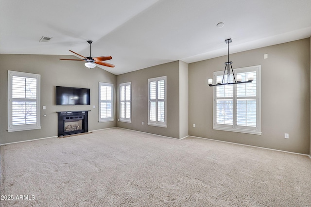 unfurnished living room with visible vents, carpet floors, lofted ceiling, a fireplace with flush hearth, and ceiling fan with notable chandelier