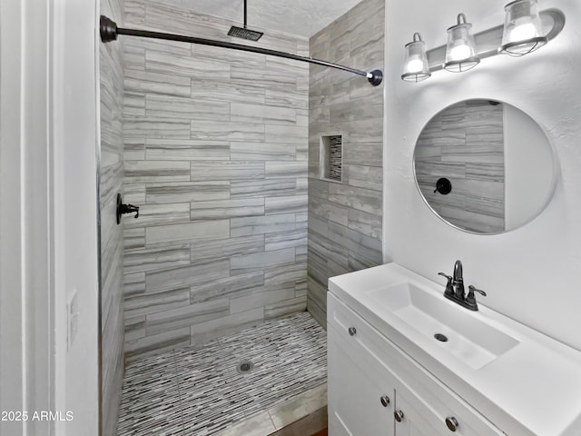 bathroom featuring visible vents, a tile shower, and vanity