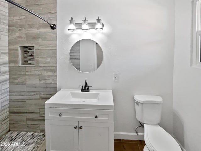 bathroom with a tile shower, vanity, toilet, tile patterned floors, and baseboards