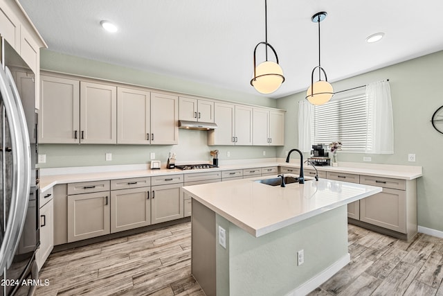 kitchen featuring sink, an island with sink, pendant lighting, light hardwood / wood-style floors, and appliances with stainless steel finishes