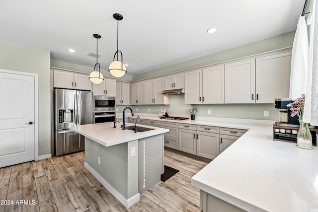 kitchen with stainless steel appliances, a kitchen island with sink, sink, pendant lighting, and light hardwood / wood-style floors