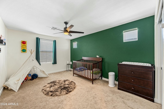 carpeted bedroom with ceiling fan and a nursery area