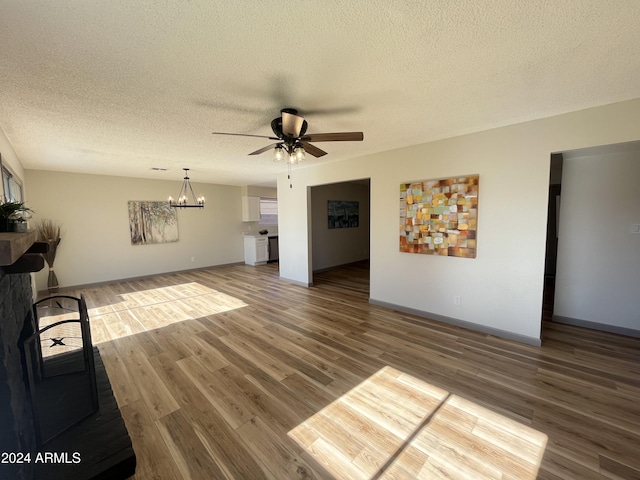 unfurnished living room featuring ceiling fan with notable chandelier, wood-type flooring, and a textured ceiling