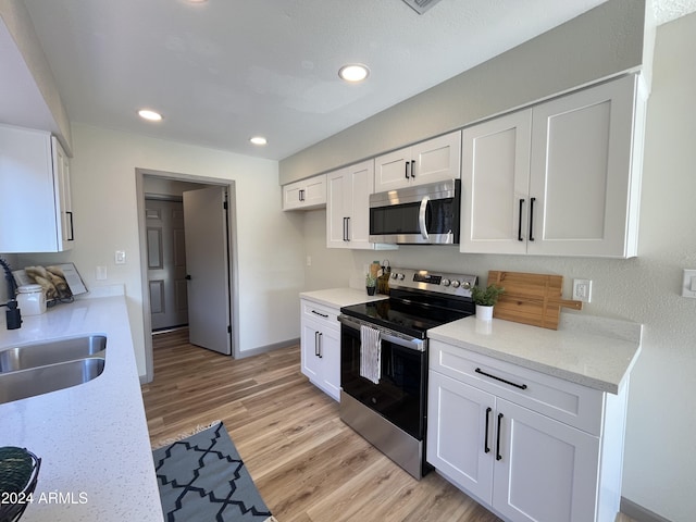 kitchen featuring white cabinets, sink, light hardwood / wood-style flooring, light stone countertops, and stainless steel appliances