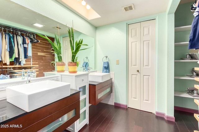 bathroom featuring hardwood / wood-style flooring, vanity, wooden walls, and a skylight