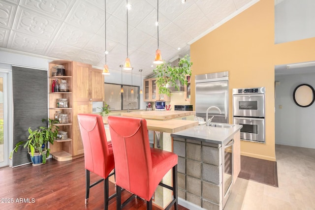 kitchen featuring sink, a kitchen island with sink, stainless steel appliances, a kitchen bar, and decorative light fixtures