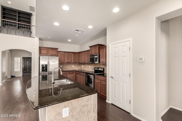 10910 E Sebring Ave, Mesa, AZ 85212 - kitchen featuring stainless steel appliances, arched walkways, dark stone countertops, a center island with sink, and tasteful backsplash