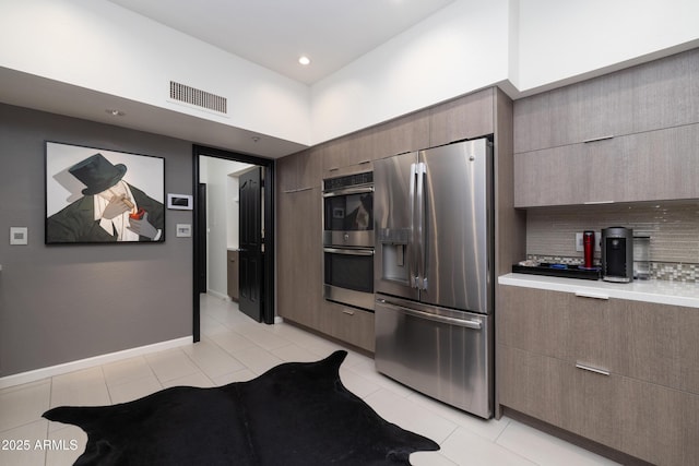 kitchen featuring tasteful backsplash, a towering ceiling, stainless steel appliances, and light tile patterned floors