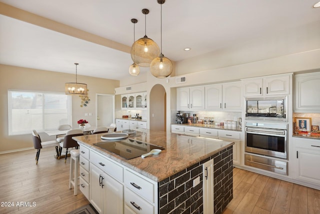 kitchen featuring light stone countertops, a kitchen island, oven, white cabinets, and electric stovetop