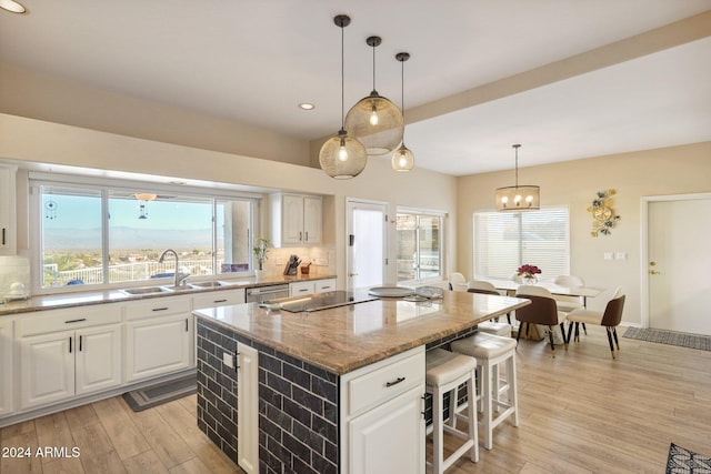 kitchen with light stone countertops, a center island, white cabinetry, and sink