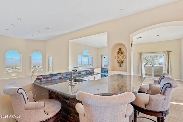 kitchen with stone counters, sink, kitchen peninsula, light hardwood / wood-style floors, and a breakfast bar