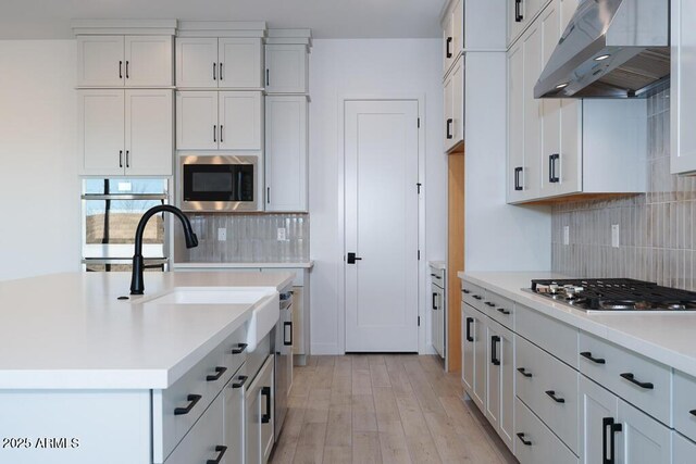 kitchen with white cabinetry, wall chimney range hood, stainless steel appliances, and light hardwood / wood-style floors