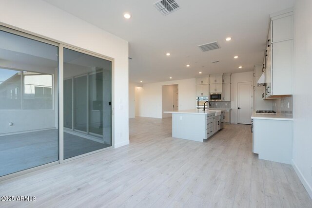 kitchen featuring a center island with sink, light hardwood / wood-style flooring, tasteful backsplash, stainless steel microwave, and sink