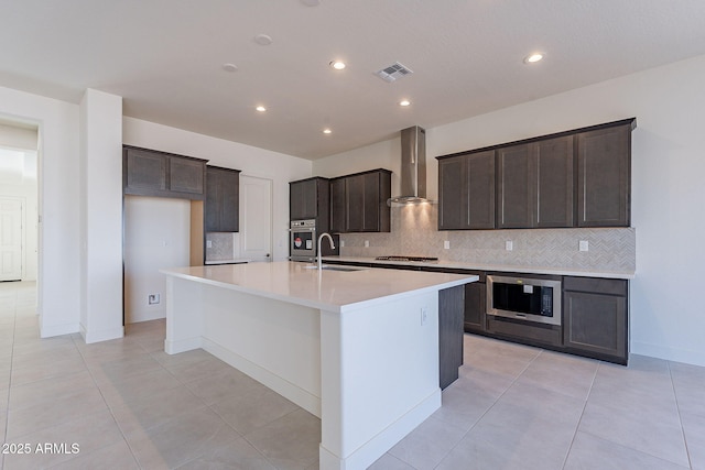 kitchen with sink, light tile patterned flooring, a center island with sink, wall chimney range hood, and appliances with stainless steel finishes