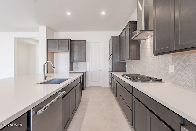 kitchen with appliances with stainless steel finishes, light tile patterned floors, wall chimney exhaust hood, sink, and dark brown cabinets