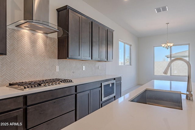 kitchen featuring hanging light fixtures, wall chimney range hood, an inviting chandelier, appliances with stainless steel finishes, and sink