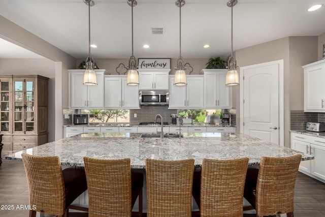 10542 W Electra Ln, Peoria, AZ 85383 - kitchen with a sink, backsplash, stainless steel microwave, a center island with sink, and white cabinetry