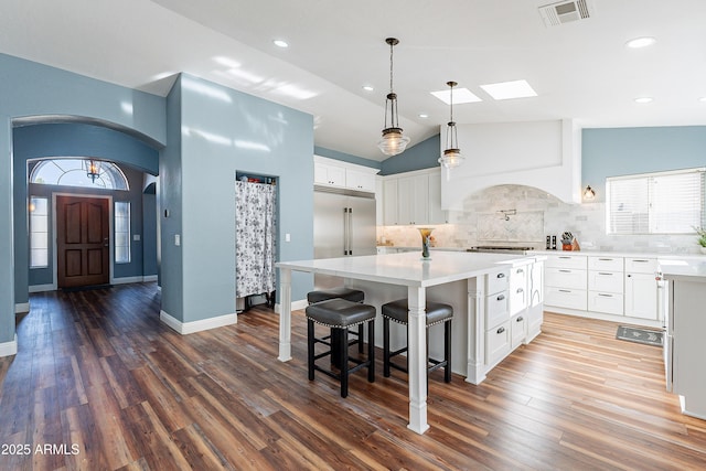 kitchen featuring vaulted ceiling, custom range hood, backsplash, white cabinetry, and a center island with sink