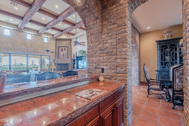 kitchen featuring a towering ceiling, coffered ceiling, a large fireplace, beam ceiling, and light tile patterned flooring