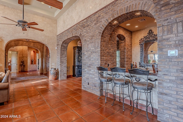 kitchen featuring tile patterned floors, ceiling fan, beamed ceiling, and a towering ceiling