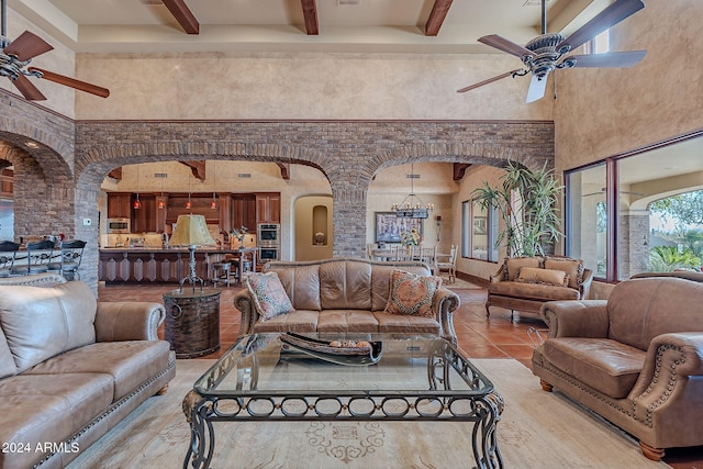 living room with ceiling fan with notable chandelier, beam ceiling, a towering ceiling, and light tile patterned flooring