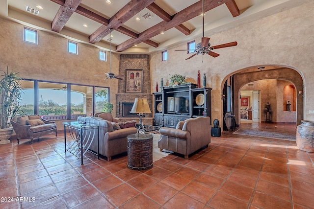 tiled living room with beamed ceiling, ceiling fan, a towering ceiling, and a brick fireplace