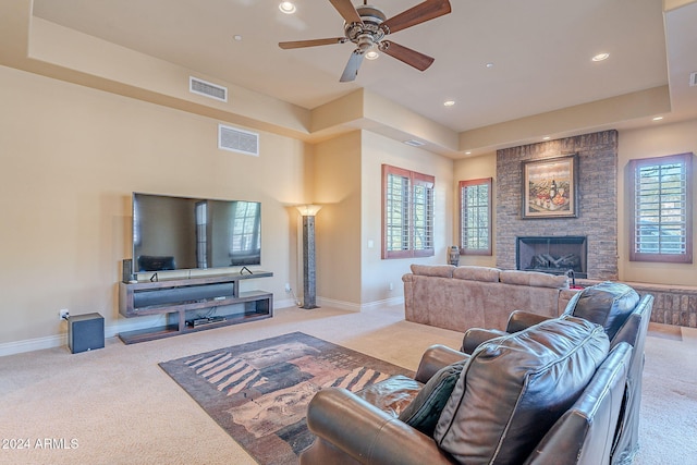 living room featuring light carpet, a tray ceiling, ceiling fan, and a fireplace