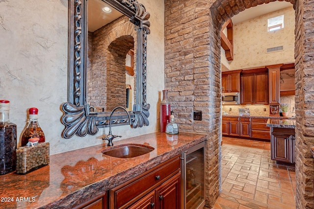 interior space with stainless steel microwave, dark stone counters, sink, a towering ceiling, and beverage cooler