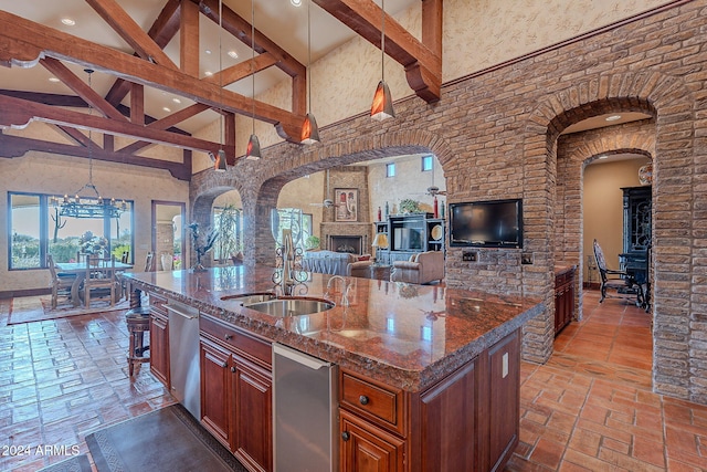 kitchen with dark stone counters, a large fireplace, an island with sink, and pendant lighting