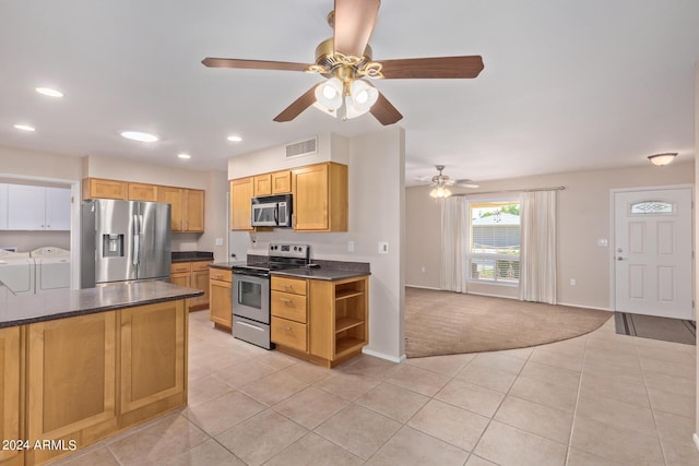 kitchen with light tile patterned floors, light colored carpet, dark countertops, appliances with stainless steel finishes, and washer and dryer