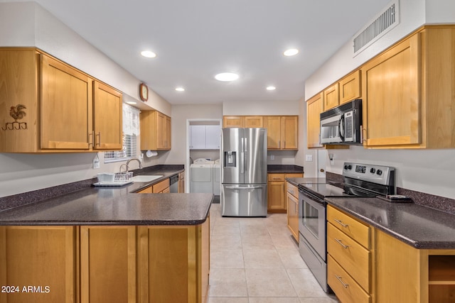 kitchen featuring appliances with stainless steel finishes, washer and clothes dryer, sink, light tile patterned floors, and kitchen peninsula